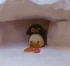 a small toy penguin sitting in the corner of a room with snow on the ground