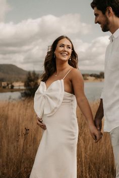 a man and woman holding hands walking through tall grass