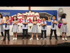 children in school uniforms stand on stage with their arms crossed and one child is holding a balloon