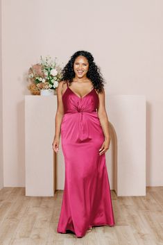 a woman in a pink dress standing next to a vase with flowers on the wall