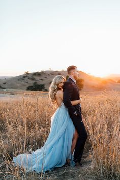 a man and woman are standing in the middle of a field with tall grass at sunset