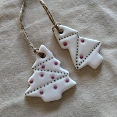 two ceramic christmas trees are hanging from twine strings on a white fabric background with pink dots