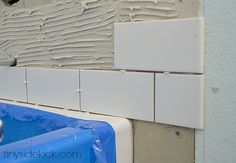 an unfinished bathroom wall with white tiles and blue water in the bathtub that is being repaired