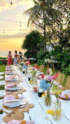 a long table is set up with plates and flowers in vases for an outdoor dinner