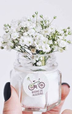 a person holding a glass jar with white flowers in it and a sticker on the lid