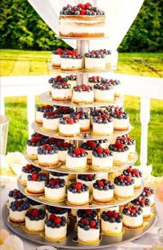 a tiered cake with cupcakes and berries on it is sitting on a table