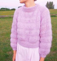 a woman wearing a purple sweater standing in the grass