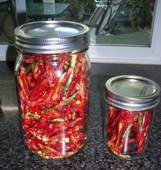 two jars filled with red peppers sitting on top of a counter