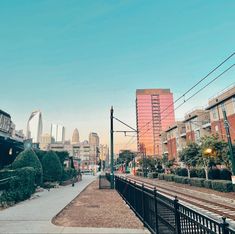 a train station with people walking on the platform and buildings in the background at sunset