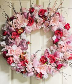 a wreath with pink and red flowers hanging on a door