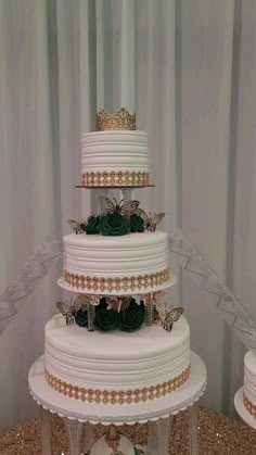 a three tiered white wedding cake with green flowers on top and gold trimmings