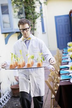 a man in white lab coat carrying trays with small food items on top of it