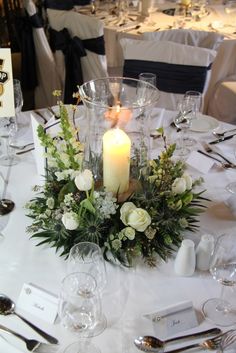 the table is set with white flowers, candles and place settings for an elegant dinner