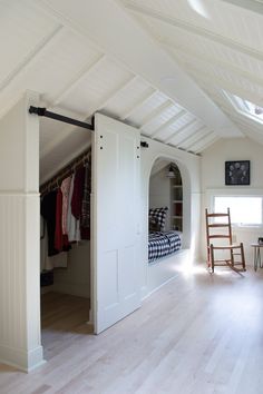 an attic bedroom with white walls and wood flooring, closet doors open to reveal a bed