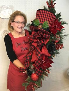 a woman is holding a christmas wreath with pine cones and red plaid ribbon on it