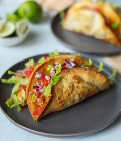 two black plates topped with tacos and salad on top of a white tablecloth