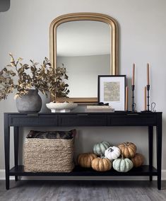 a black console table with pumpkins on it and a mirror in the corner next to it