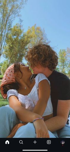 a man and woman sitting on the ground kissing each other with trees in the background