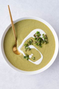 a white bowl filled with broccoli soup next to a wooden spoon on top of a table