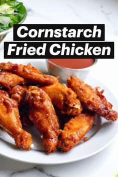 a white plate topped with fried chicken wings next to a bowl of sauce and salad