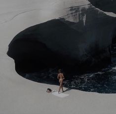 a woman walking on the beach next to a large rock and small body of water