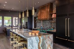 a large kitchen with marble counter tops and gold pendant lights hanging from the ceiling over the island