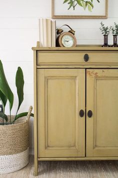 a small yellow cabinet sitting next to a potted plant and a clock on top of it