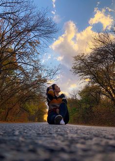 a woman sitting on the ground with her legs crossed in front of trees and clouds