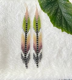 two pairs of beaded earrings on top of a white blanket next to a green leaf