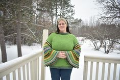 a woman wearing a green sweater standing on a porch in the snow with her arms crossed