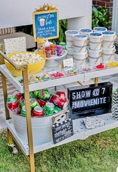 an outdoor movie party with popcorn, soda cans and snacks on a cart in the grass