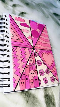 a spiral notebook with pink and purple designs on the cover, sitting on a bed