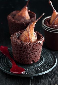 three chocolate desserts with apples in the middle on a black plate and red sauce drizzled around them