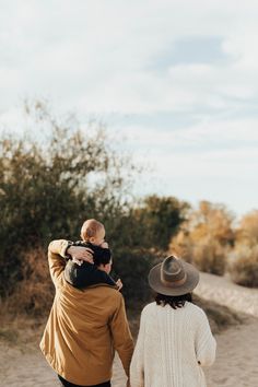 a man and woman walking down a dirt road with a baby in their arms,