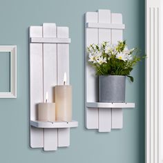 two white wall mounted shelves with candles and flowers in the middle, one holding a potted plant