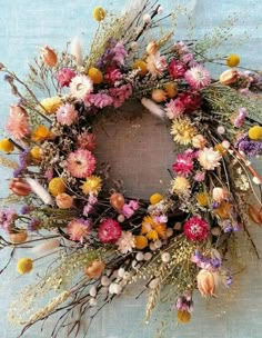 a wreath made out of dried flowers on a blue tablecloth with white and yellow feathers