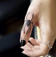 a woman's hand with a spider tattoo on her left thumb and ring finger