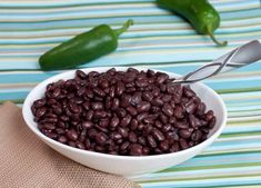 a white bowl filled with black beans next to green peppers on top of a table