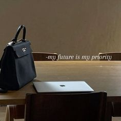 a black purse sitting on top of a wooden table next to a laptop and chair