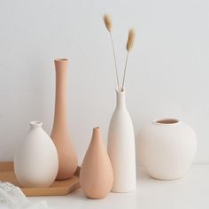 three white vases and two brown ones on a wooden tray next to each other