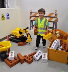 a young boy standing in front of construction equipment on the floor with blocks laid out around him