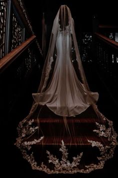 the bride is walking down the stairs wearing her wedding dress and veil with flowers on it