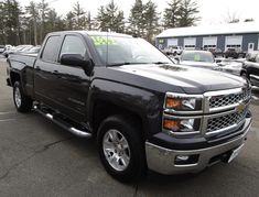 a black truck is parked in a lot with other cars and trucks behind it that are for sale