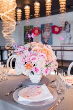 a vase filled with pink and white flowers on top of a dining table next to silverware