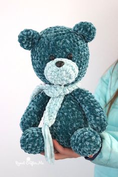 a small blue teddy bear with a white ribbon around it's neck, held by a woman