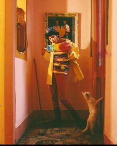 a man in clown makeup standing next to a cat and looking at a painting on the wall