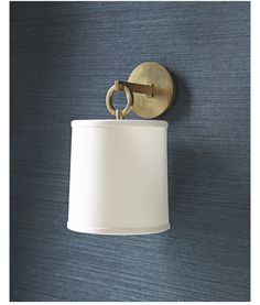 a wall light with a white shade hanging from it's side against a blue wall