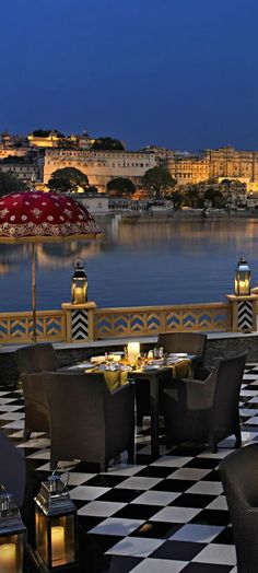 an outdoor dining area with tables, chairs and umbrellas overlooking the water at night