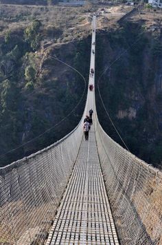 people walking across a suspension bridge in the mountains