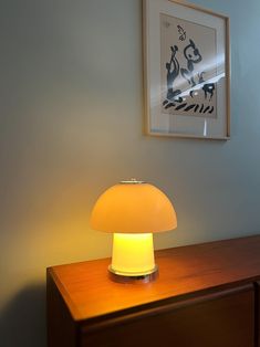 a lamp is sitting on top of a wooden dresser next to a framed art piece